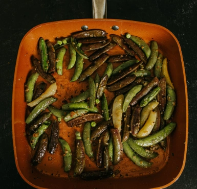 A frying pan with green beans and peas.