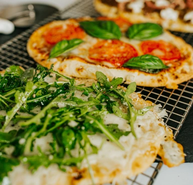 Three pizzas on a cooling rack with herbs and tomatoes.