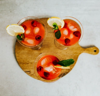 Three glasses of raspberry lemonade on a wooden cutting board.
