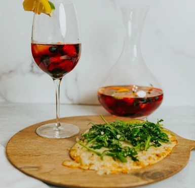 A glass of sangria and a slice of pizza on a wooden board.